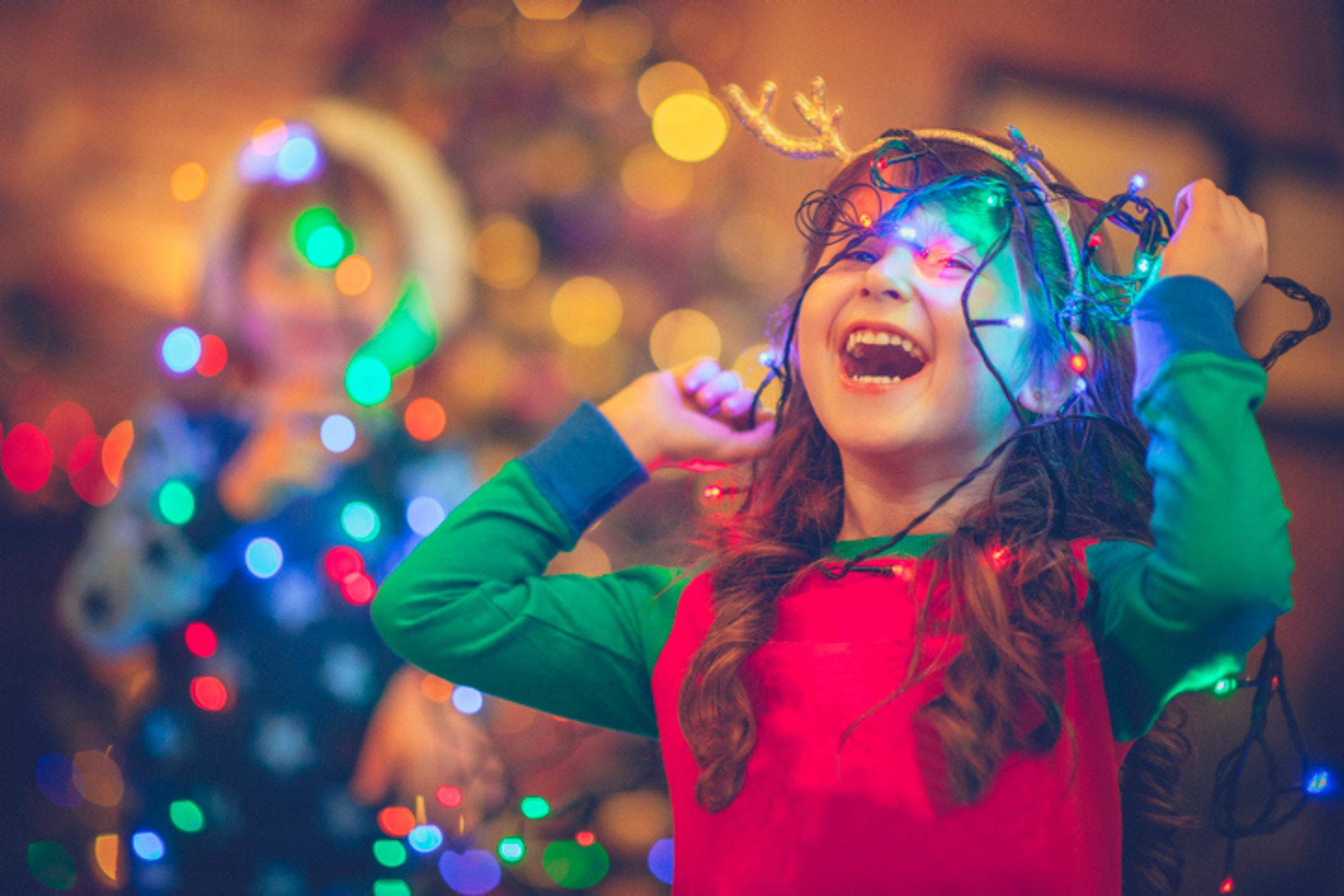 Young girl with fairy lights wrapped over her head with a massive smile